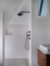 A white tadelakt plaster shower with a niche shelf and matte black shower head and fixtures