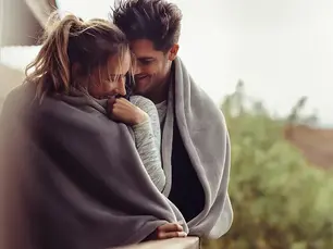 Donna e uomo abbracciati avvolti in una coperta, in un gesto intimo e protettivo, simbolo del potere di ricevere amore, lasciarsi andare e accogliere con fiducia la connessione emotiva