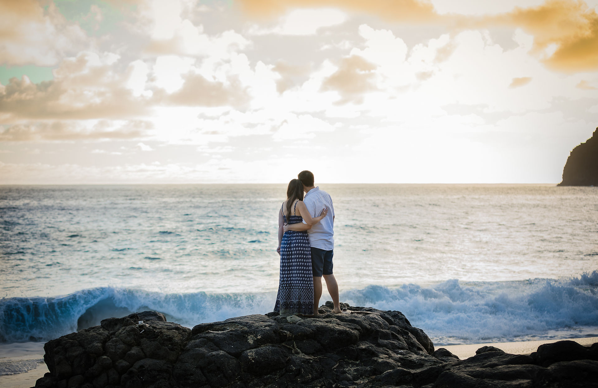 couple watching the waves while standing on a rock
