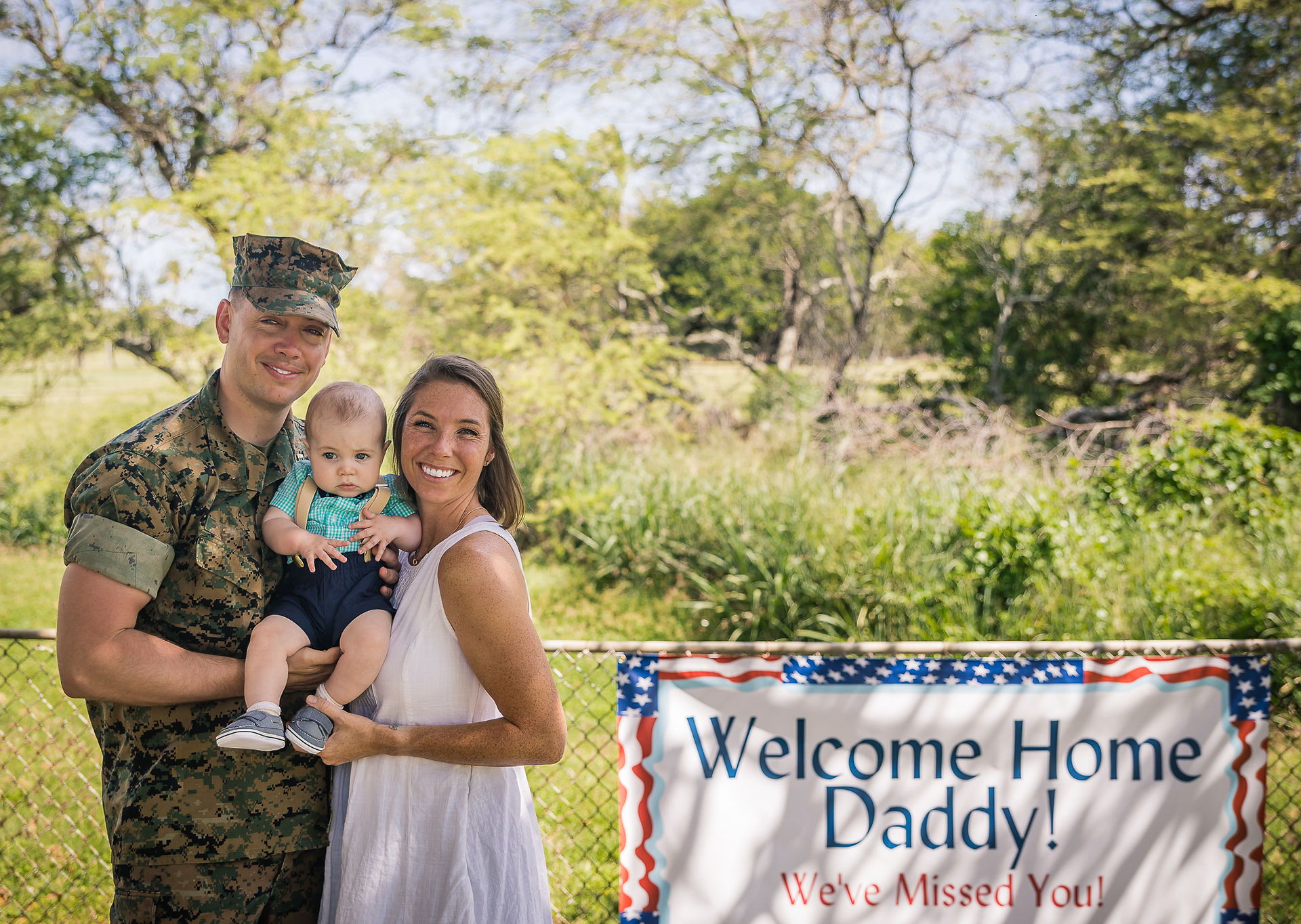 Family of three pose next to their homecoming sign