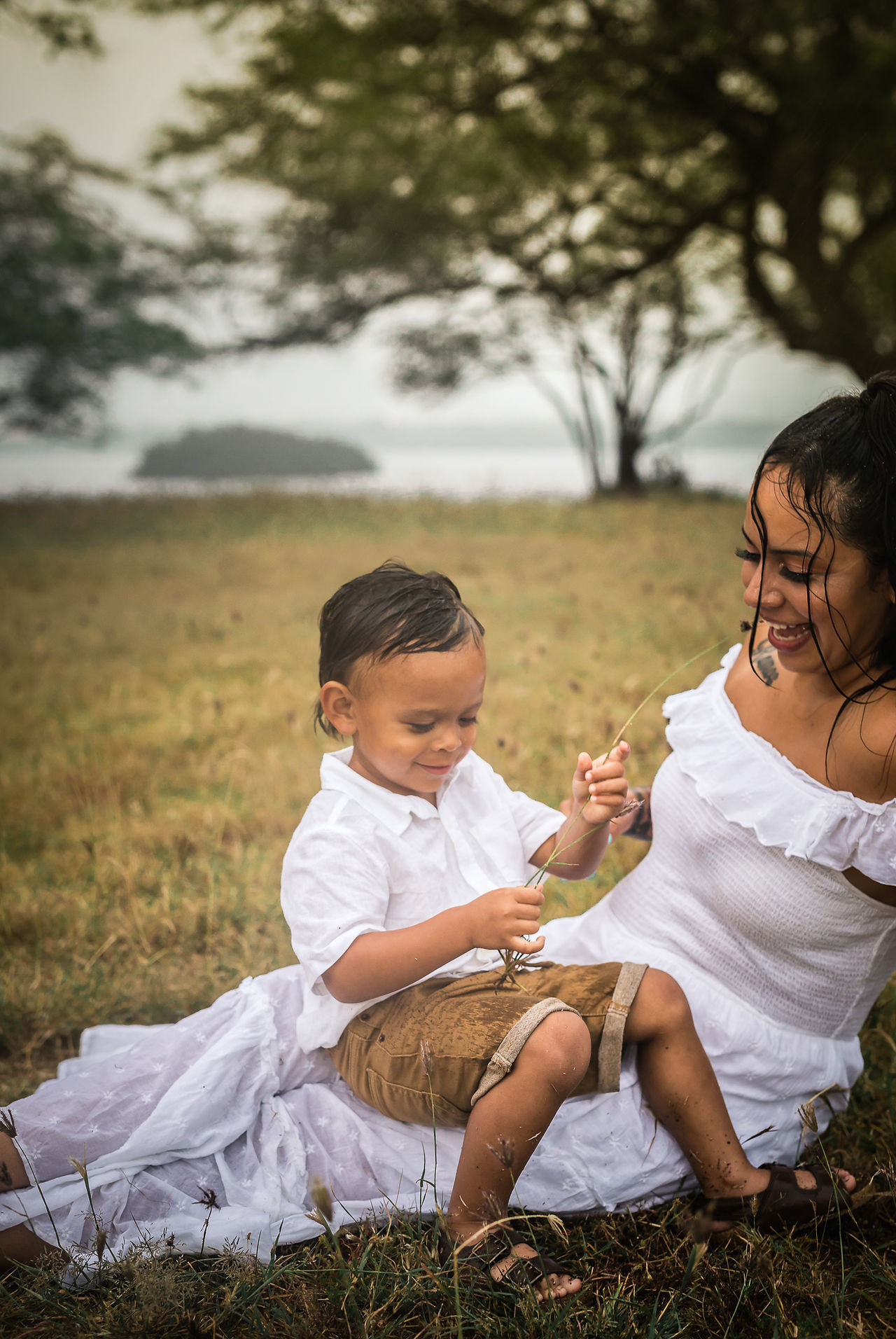 Son sitting on mom's lap playing with a straw of weed as it's raining