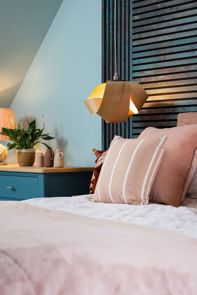 Wooden pendant light against blue slatted distressed feature wall, creating warm glow in bedroom