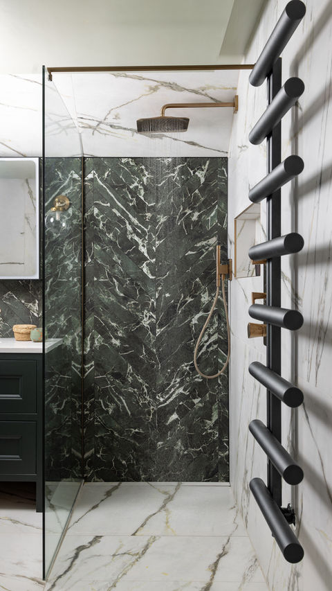 Green and white marble bathroom with freestanding bath, dark green vanity, walk-in shower and brass fittings.