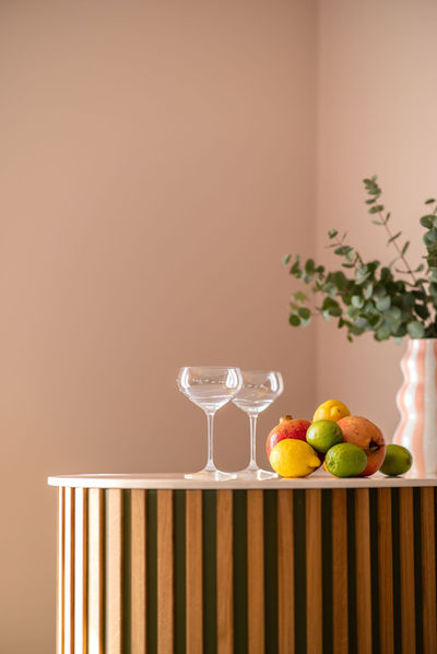 Curved oak fluted bar styled with coupe glasses, citrus fruits, and a wavy vase on blush pink walls. Retro chic modern interior design by Leisha Norman, carpentry by Paul Handley Bespoke