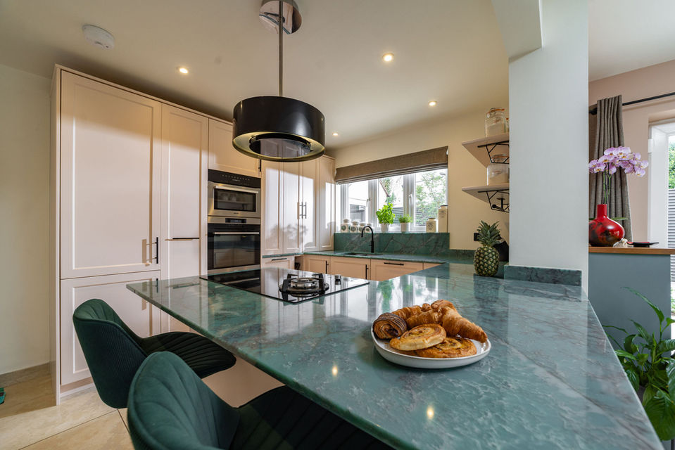 Open plan kitchen and dining space in Southampton with teal green stone worktop, cane back chairs and colourful patterned curtains, styled by Hampshire interior designer.
