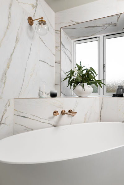 Brushed brass wall-mounted basin taps against dark green marble-effect herringbone tiles.