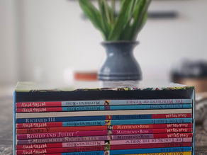Stack of colorful children's books on Shakespeare on a wooden table, with titles visible. The mood is educational and whimsical.