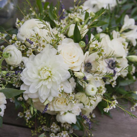 White and cream flowers with green leaves on a wooden surface. The bouquet includes roses and dahlias, creating an elegant and tranquil setting.