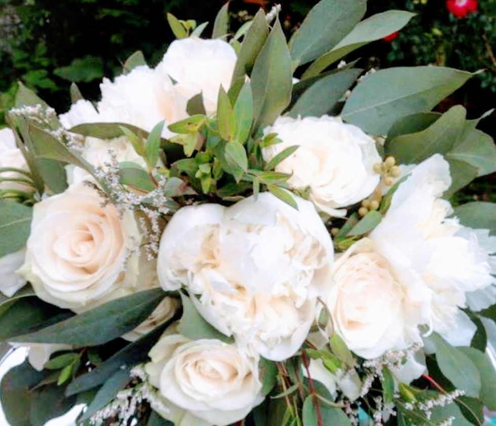 White roses and peonies with greenery arranged in a bouquet on a reflective surface. Soft, natural colors create a serene mood.