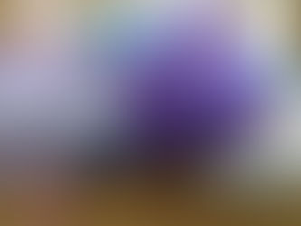 Purple flowers, violets, on notebooks with pink and lavender ribbons, set on wood. Background is a blurred mix of blue and brown tones.