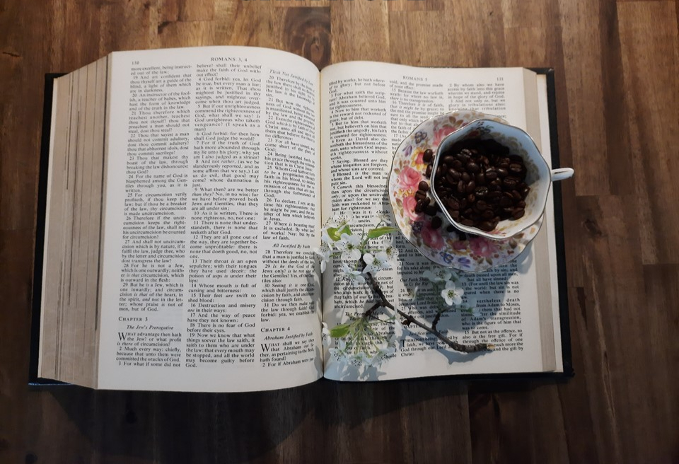 Otwarta stara Biblia z gałązką kwitnącej wiśni i piekną filiżanką na talerzyku jako symbol spotkania ze Słowem przy porannej kawie
