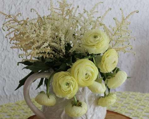 yellow ranunculus flowers bouquet in a white vase standing on a birch slate on a table. 
