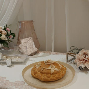 Stół udekorowany bochenkiem chleba - chleb życia, który zaspokaja pragnienia serca na zawsze, z ozdobami, bukietem kwiatów, świecznikami i kremowymi zasłonami w tle. Elegancka, delikatna atmosfera. symbol obfitości i Błogosławieństwa