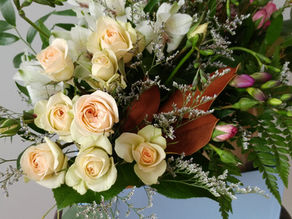 Bouquet of pale roses and pink buds with green leaves in a blue box on a wooden stool. Light gray background, elegant and serene mood.
