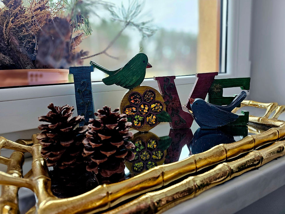 Decorative "LOVE" letters with birds sit on a reflective tray, surrounded by pinecones. A window with trees in the background is visible.