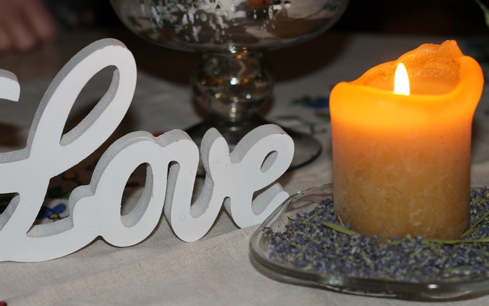 A yellow burning candle and white wooden LOVE sign symbolizing St. Joseph's virtues.