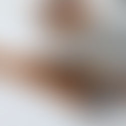 Łyżeczka pełna mielonego cynamonu na tle kilku lasek cynamonu. Obok przezroczysta miska z przyprawą. Jasne tło.