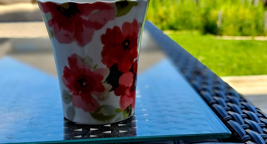 A flowery cup of coffee standing on a glass table in the backyeard on a sunny summer morning - invitation for reflection with the Bible.