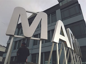 Large custom 3D metal letters on a steel framework being installed for a commercial building landmark.