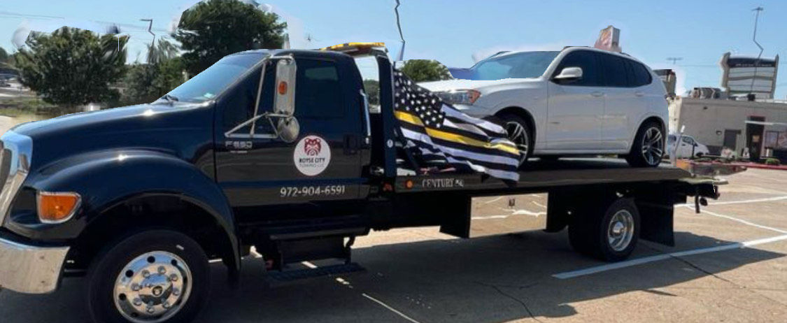 Tow truck operator securing a vehicle for transport on a flatbed tow truck