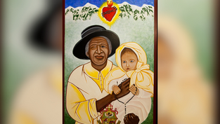Woman in black hat and beige robe holds a baby in white attire with a rosary. Heart symbol above. Green background with mountains.