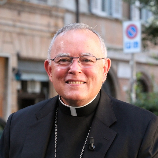 Monsignor Bernie Schmidt gives a blessing at the altar, surrounded by candles and a gathering.