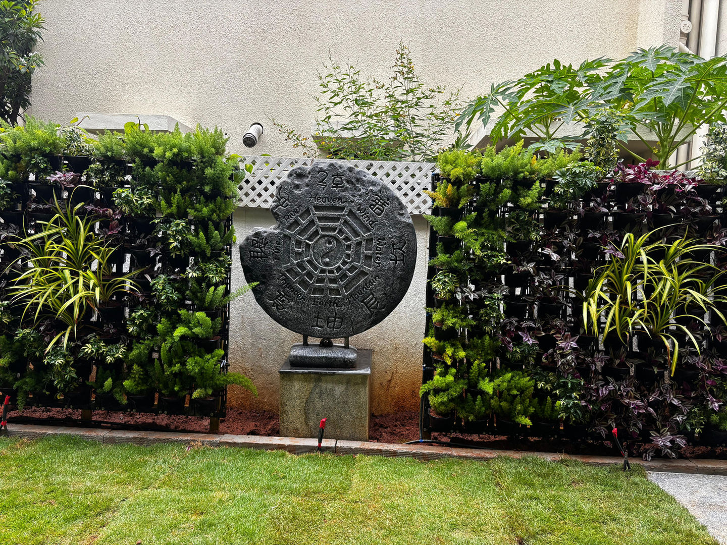 Stone sculpture in a backyard garden, surrounded by green plants, Anantha Landscape.