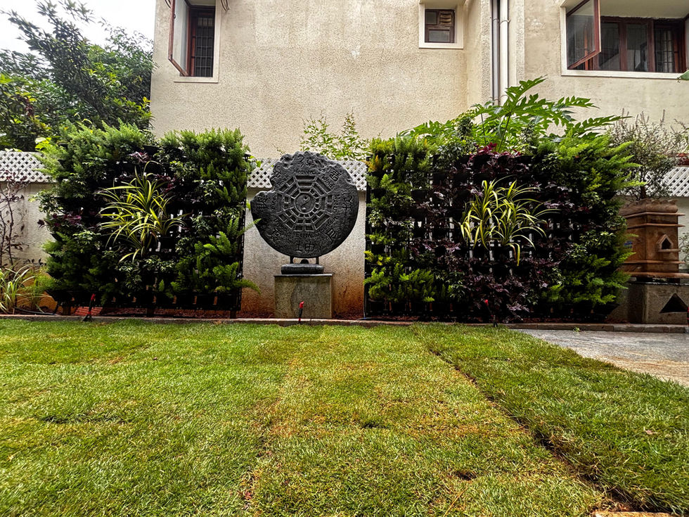 Sculpture in backyard garden with green foliage and building background, Anantha Landscape.