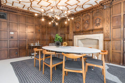 Conference room with original carved wood paneling, stone fireplace, and modern chandelier at 80 Eighth Avenue in Chelsea.