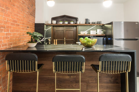 Office kitchen with exposed brick, black marble island, and brass bar stools at 80 Eighth Avenue.