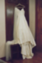 Elegant ivory wedding dress with veil on a hanger. Draped over a bench, brown wood panel background, evokes a serene, romantic mood.