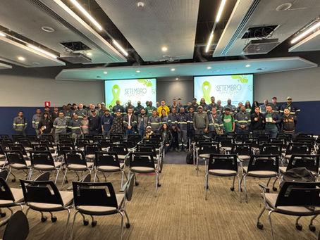 Grupo de trabalhadores posa em auditório vazio; telões exibem Setembro Amarelo com laço amarelo, clima de campanha.