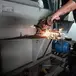 Operário corta metal de máquina HIGROTEC com esmerilhadeira, gerando faíscas em oficina industrial.