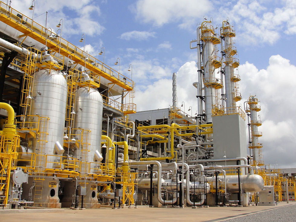 Planta industrial com tanques e tubulações metálicas amarelas sob céu azul; estruturas altas e limpas, sem pessoas.