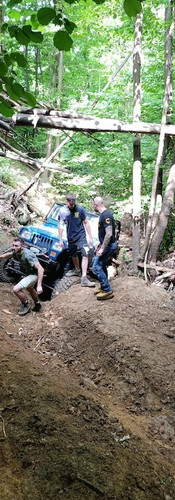 ragazzi che aiutano la jeep incastrata nel canale, tirando il cavo del verricello