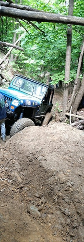 Jeep blu elettrico impegnato a salire in un canale nel sottobosco