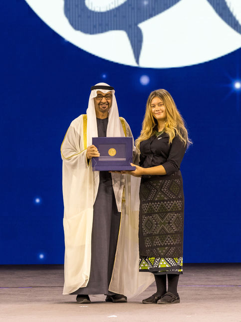 His Highness (HH) Sheikh Mohammed bin Zayed Al Nahyan presenting an award to a female winner on a stage in a black and gold dress