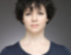 Headshot of Natasha Conti. A brunette with short curly hair wearing a black shirt.