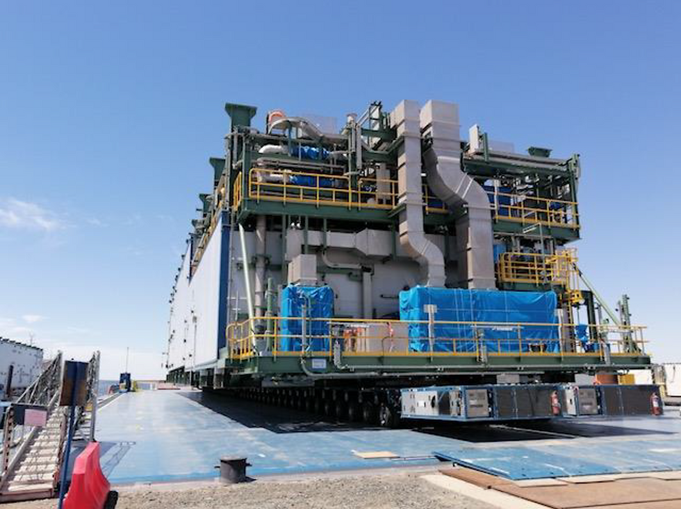 Eye-level view of a modular fabrication yard with heavy lift cranes and marine transport vessels docked