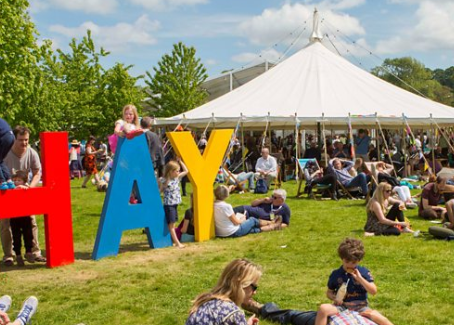 Large H A Y letters displayed in red, blue and yellow colours with a festival tent in the background