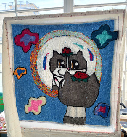 Hand-tufted rug artwork of Mooncake the cat wearing a strawberry hat and looking into a mirror, surrounded by colorful stars and whimsical kawaii-inspired objects on a blue background. Plush yarn textile art featuring cute fantasy imagery, vibrant colors, and soft handmade textures.