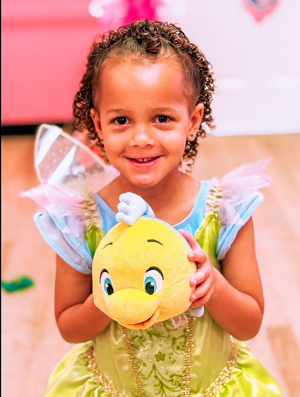 A girl in a princess dress smiles and holds a stuffed fish