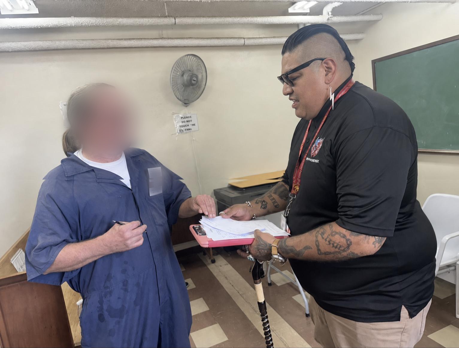 A VetPhoenix peer support specialist reviews paperwork with an incarcerated veteran, whose face is obscured.