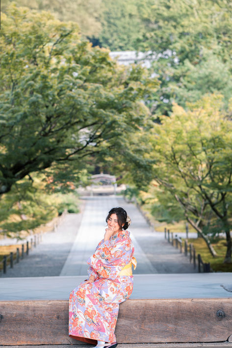 Woman in a pink kimono seated by a peaceful Kyoto temple path.
