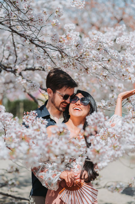 Couple smiling together among soft white cherry blossoms.