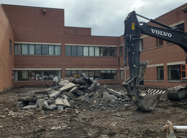 A Volvo excavator performing demolition work between large brick commercial buildings