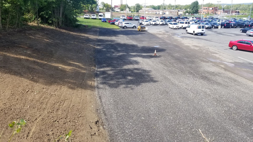 A portion of a parking lot covered with crusher run with cars parked in the distance