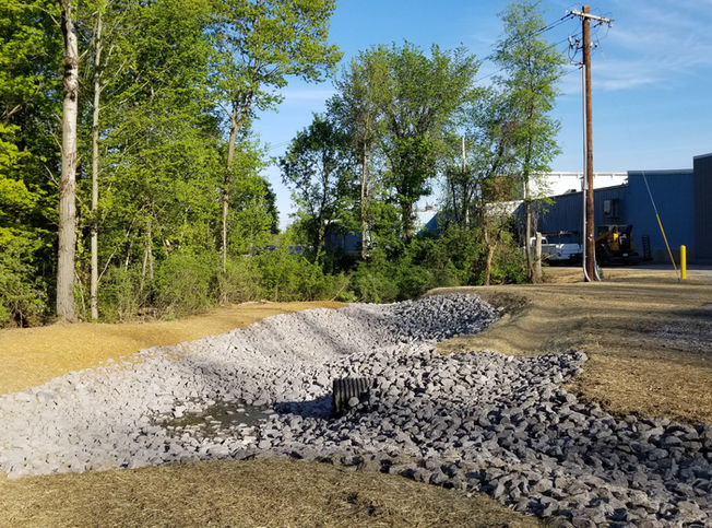 A section of ground dug out by an excavator is covered with stone around a drainage grate