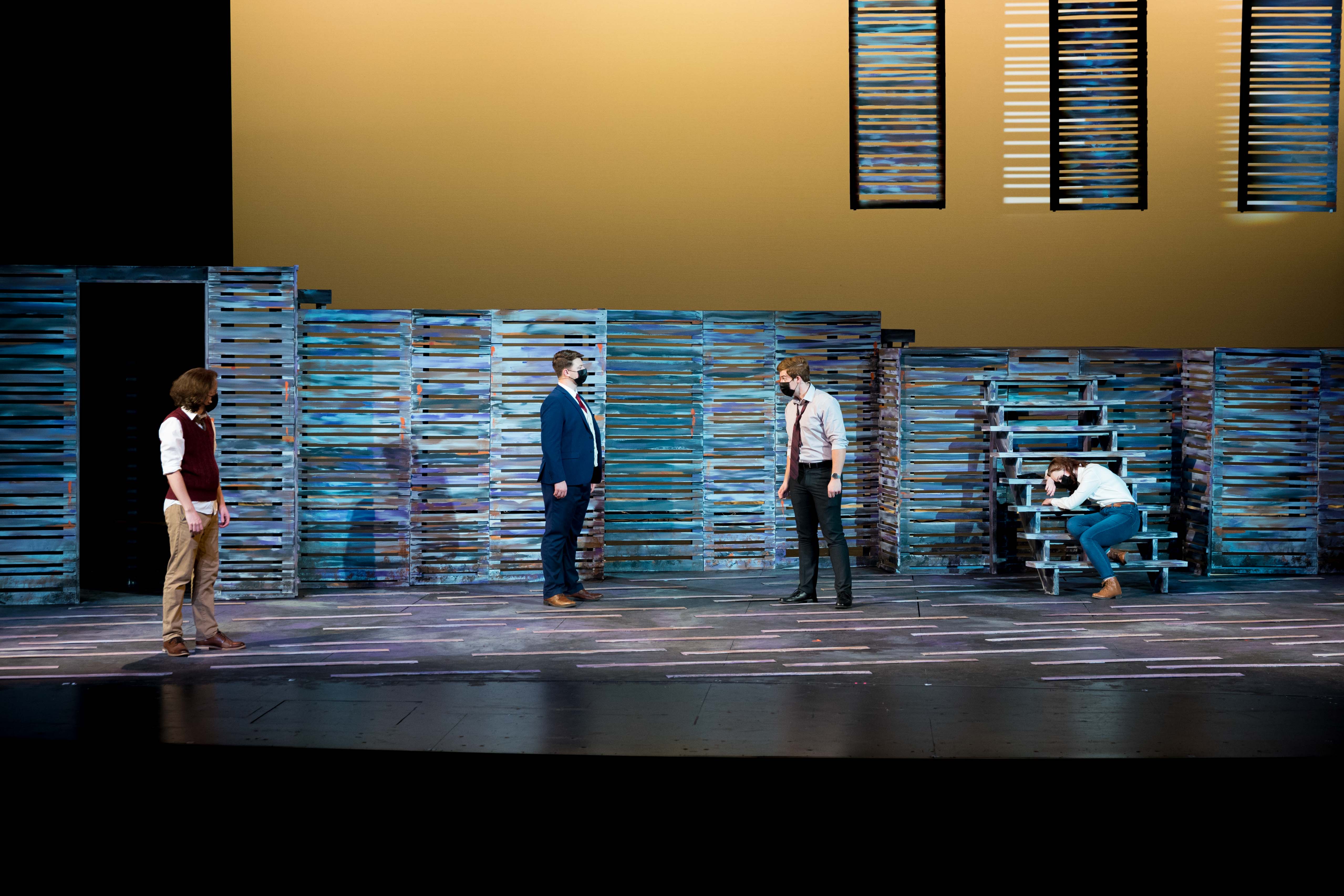 Four people on a stage under yellow light, one sitting on a staircase.