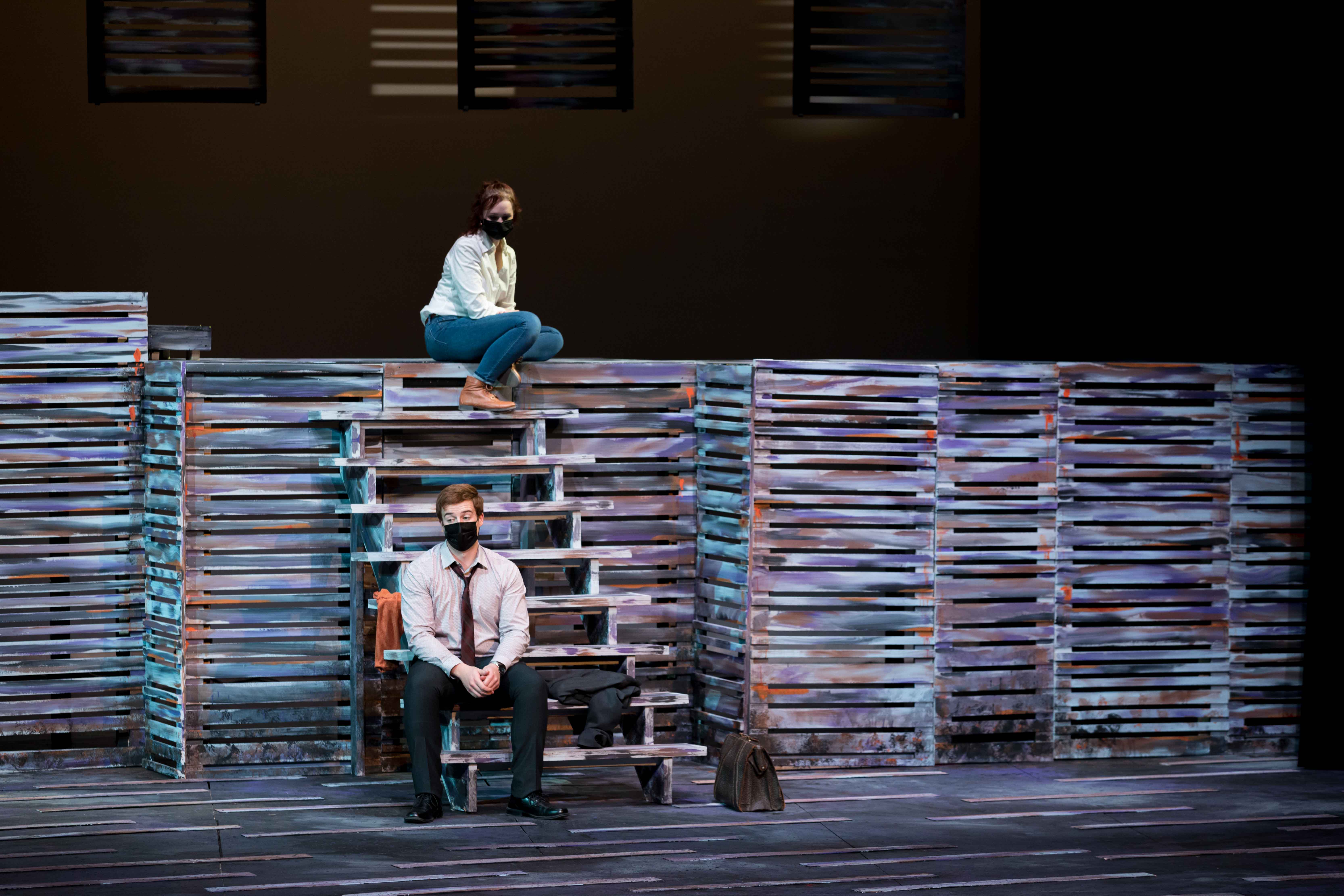 Two people on a stage, one on a raised platform, one on a set of stairs.